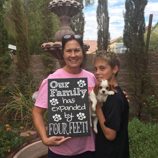 A woman and her son holding a puppy beside a sign reading Our Family Has Expanded By Four Feet