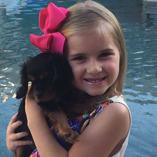 A young girl at a pool holding her new puppy, wearing a pink bow